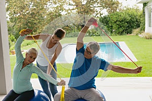 Female trainer assisting active senior couple to exercise with resistance band in the porch