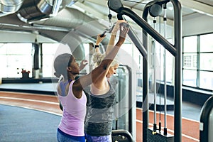 Female trainer assisting active senior woman on lat pulldown machine in fitness studio