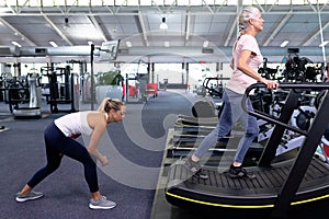 Female trainer assisting active senior woman on treadmill in modern sports center