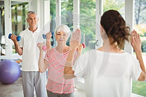 Female trainer assisting senior couple in performing exercise