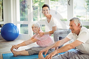 Female trainer assisting senior couple in performing exercise