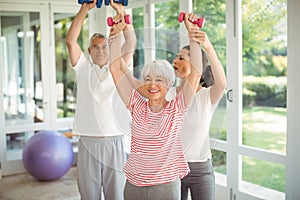 Female trainer assisting senior couple in performing exercise
