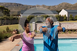 Female trainer assisting senior man in performing exercise