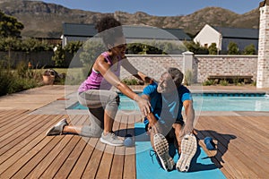 Female trainer assisting senior man in performing exercise