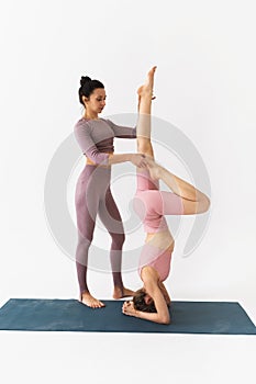 A female trainer helps a student to perform the Shirshasana exercise, an inverted asana