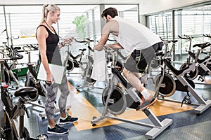 Female trainer looking at stopwatch and man using exercise bike