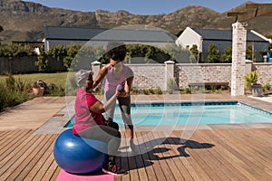 Female trainer training senior woman in performing exercise in the backyard