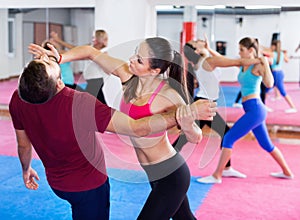 Female is training self-defence moves in pair with trainer in sporty gym.