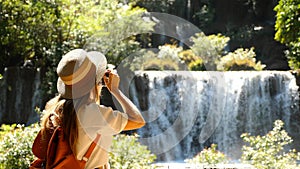 Female travel blogger with photo camera shooting amazing tropical waterfall in Asia journey. Cinematic and inspiration