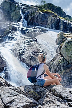 Female traveler admiring the view of the waterfall on a sunny day.