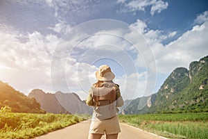 Female traveler backpacking on tourist road with sky and mountains in front