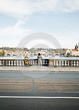 Female traveler dressed in gray coat standing on the bridge above Vltava river