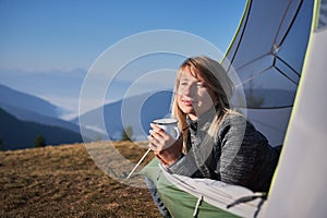 Charming young woman hiker resting in camp tent in mountains.