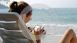 Female traveler scrolls through photos on phone while sunbathing