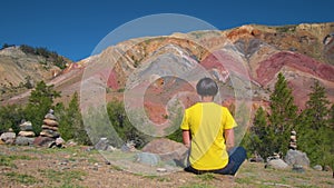 A female traveler sits on a huge tree stump and meditates against the beautiful mountains