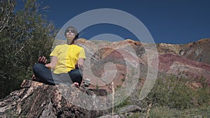 A female traveler sits on a huge tree stump and meditates against the beautiful mountains