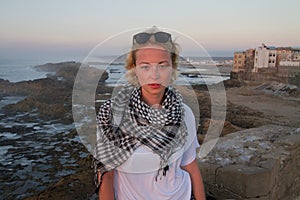 Female traveler standing on city fortress wall of Essaouira, Morocco in sunset.