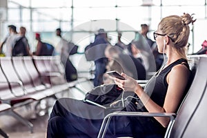 Female traveler talking on cell phone while waiting to board a plane at departure gates at asian airport terminal.