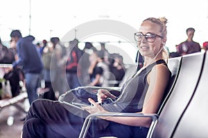 Female traveler using her cell phone while waiting to board a plane at departure gates at asian airport terminal.