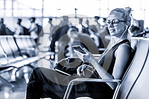 Female traveler using her cell phone while waiting to board a plane at departure gates at asian airport terminal. Blue