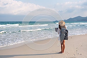 A female traveler using and working on laptop computer while walking on the beach