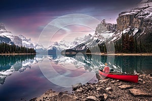 Female traveler in winter coat rowing a red canoe in Spirit Island on Maligne Lake at the sunset