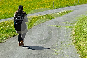 Female traveller with backpack walking along trail of green road