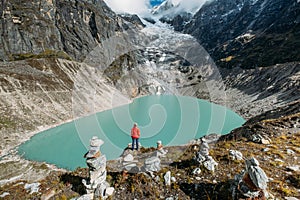 Female trekker dressed bright red jacket on the rock enjoying a glacier falling in high altitude Sabai Tso glacial lake cca 4350m