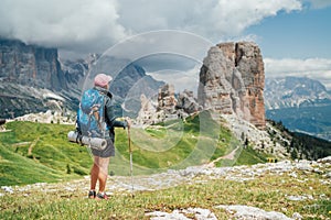 Female trekker walking with backpack and trekking poles by green mountain hill and enjoying the picturesque Dolomite Alps Cinque