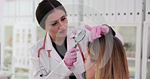 Female trichologist examines condition of weak hair on patient head using dermatoscope and magnifying glass