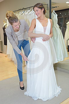 Female trying wedding dress in shop with women assistant