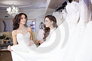 Female trying on wedding dress in a shop with women assistant.