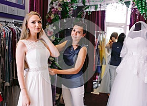 Female trying on wedding dress in a shop with women assistant.