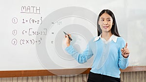 Female tutor standing in front of whiteboard and writing math equations on board to explaining new lesson