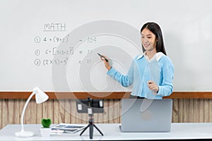 Female tutor standing in front of whiteboard and writing math equations on board to explaining new lesson