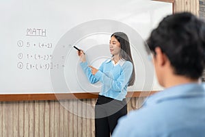 Female tutor standing in front of whiteboard and writing math equations on board to explaining for student