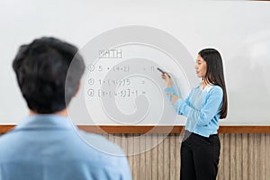 Female tutor standing in front of whiteboard and writing math equations on board to explaining for student