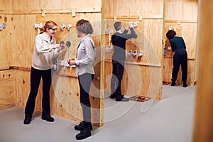 Female Tutor With Trainee Electricians In Workshop Studying For Apprenticeship At College