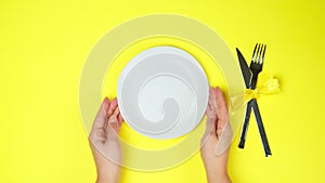 Female two hands put white empty plates with a metal knife and fork. top view