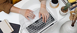 Female typing on laptop keyboard on white table with diary book, books and decorations