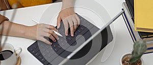 Female typing on tablet keyboard on worktable with coffee cup, books and decorations