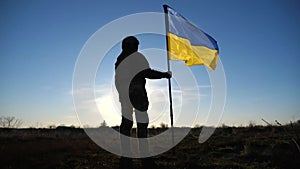 Female ukrainian army soldier holding waving flag of Ukraine with sun flares at background. Woman in military uniform