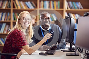 Female University Or College Student Working At Computer In Library Being Helped By Tutor