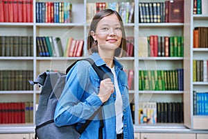 Female university student with backpack, inside library of educational building