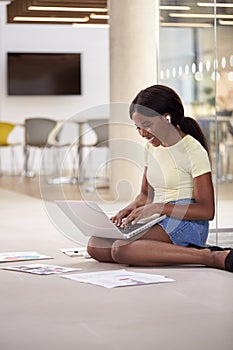 Female University Student On Floor Of College Building With Laptop Listening To Music On Earbuds