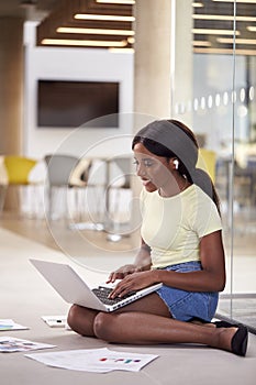 Female University Student On Floor Of College Building With Laptop Listening To Music On Earbuds