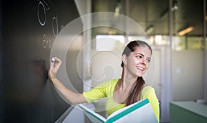 Female university student in front of a blackboard solving a problem