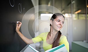 Female university student in front of a blackboard solving a problem