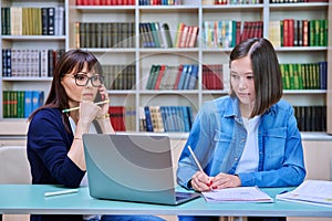 Female university student with teacher preparing for exam, inside library