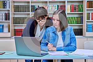 Female university student with teacher preparing for exam, inside library